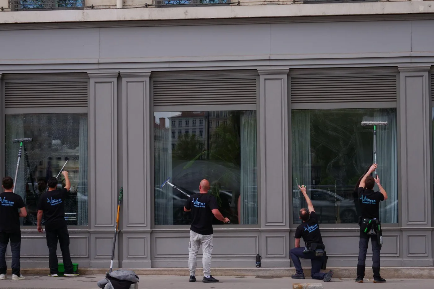 Cinq laveurs de vitres VitClean nettoyant une façade vitrée à la perche, à Lyon.
